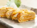 Délicieux oeuf japonais roulé, aux couches dorées et blanches, servi sur une assiette avec une feuille verte.