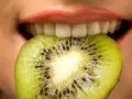 Une tranche de kiwi est mordue par des lèvres roses, ses petites graines noires contrastant avec la chair verte. Une sensation de kiwi langue qui pique.