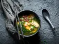 Un bol de bouillon miso fumant, garni de tofu, d'algues et de pousses rouges, prêt à être dégusté avec des baguettes.