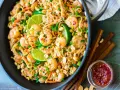 Un plat de recette pad thai crevette appétissant dans un wok, garni de crevettes, de cacahuètes, de coriandre et de quartiers de citron vert.