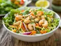Salade de nouilles thaï colorée avec crevettes, carottes râpées, oignons rouges et coriandre fraîche, servie dans un bol blanc.