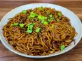 Un plat de nouilles savoureuses, enrobées d'une sauce brune appétissante, garnies de graines de sésame noir et de ciboule fraîche.
