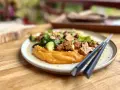 Un plat savoureux de tofu miso sur une purée de patates douces, garni de légumes verts et de graines de sésame.