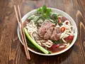 Un bol de soupe nouille de riz avec du bœuf, des germes de soja, des oignons verts et du piment rouge, prêt à être dégusté avec des baguettes.