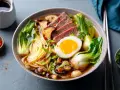 Un bol de pâte ramen savoureux avec des tranches de bœuf, un œuf mollet, des champignons et du bok choy.