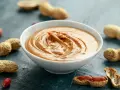 Un bol de sauce cacahuète facile, crémeuse et onctueuse, entouré de cacahuètes entières et décortiquées.