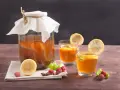 Bocal de kombucha et deux verres garnis de citron, framboises et menthe. Découvrez les kombucha bienfaits pour une boisson rafraîchissante et saine.