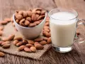 Un verre de lait d'amande frais à côté d'un bol d'amandes entières sur une surface en bois rustique.