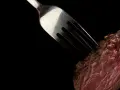 Une fourchette transperce un morceau de viande rouge, rappelant la prudence pour ceux qui ont une allergie au porc.