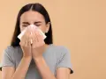 Une jeune femme se mouche dans un mouchoir en papier, le nez bouché par un rhume.