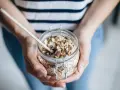 Mains de personne tenant un bocal en verre rempli de muesli maison, avec une cuillère en bois.