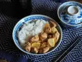 Un plat de riz blanc avec du poulet mariné sauce soja, garni de quartiers de citron. Un bol décoré et des baguettes complètent la scène.