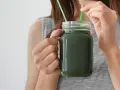 Une femme boit un smoothie vert à la spiruline, un allié pour la santé et la beauté des cheveux.