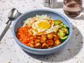 Un bol de bibimbap tofu avec riz, carottes râpées, concombre, œuf au plat et cacahuètes concassées.
