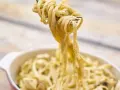 Une fourchette soulève des pâtes crémeuses, peut-être des pâtes cacahuète, d'un plat.