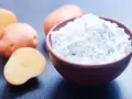 Fécule de pomme de terre dans un bol, avec des pommes de terre coupées en arrière-plan. Idéal pour savoir par quoi remplacer la fécule de pomme de terre.
