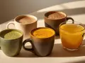 Quatre tasses de boissons colorées : matcha, curcuma, chocolat chaud et boisson dorée. Une belle alternative au café pour commencer la journée.