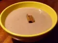 Un bol jaune contient une crème onctueuse de banane au lait de coco, garnie d'un bâton de cannelle.