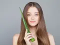 Une jeune femme aux cheveux longs tient une feuille d'aloe vera, montrant comment utiliser l'aloe vera pour une peau éclatante.