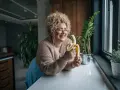 Une femme souriante avec des cheveux bouclés tient une banane, malgré une possible allergie à la banane.