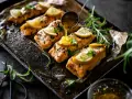 Filets de saumon sauce soja sucrée, garnis de citron et de persil, sur un plateau orné. Une louche verse la sauce.