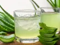 Deux verres de jus d'aloe vera à boire, entourés de feuilles d'aloe vera fraîches et de morceaux coupés.