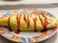 Une omelette japonaise au riz, nappée de ketchup, sur une assiette décorée de fleurs.