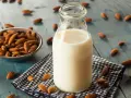 Bouteille de lait végétal d'amande, avec un bol d'amandes et des amandes éparpillées sur une table en bois bleu.