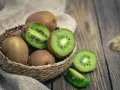Un panier de kiwis frais, certains entiers, d'autres coupés, révélant leur chair verte et leurs pépins noirs. Attention, le kiwi peut provoquer une allergie.