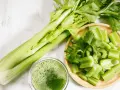 Jus de céleri frais, coupé en morceaux dans un bol en bois. Une branche entière de céleri est à côté. Attention à l'allergie céleri.