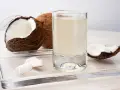 Un verre d'eau de coco, entouré de morceaux de noix de coco fraîches. Découvrez les nombreux bienfaits de l'eau de coco pour votre santé.