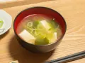 Un bol de soupe japonaise, avec du tofu et des oignons verts, servi avec des baguettes sur un plateau en bois.