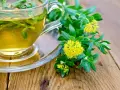 Une tasse de thé à la rhodiola, avec des fleurs jaunes et des feuilles vertes sur une table en bois. Idéal pour soulager les vertiges.
