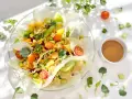 Un rouleau de printemps végétarien coloré, rempli de nouilles, carottes, concombre, pois et herbes fraîches, servi avec une sauce.