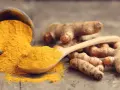 Racines de curcuma et poudre dorée sur une cuillère en bois, symbolisant le curcuma bienfait pour la santé.