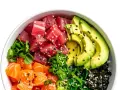 Un délicieux poke bowl avec thon, saumon, avocat, algues et sauce, garni de graines de sésame.