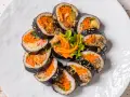 Un assortiment de makis végétariens colorés, garnis de carottes râpées, d'omelette et de légumes croquants, disposés en cercle sur une assiette blanche.