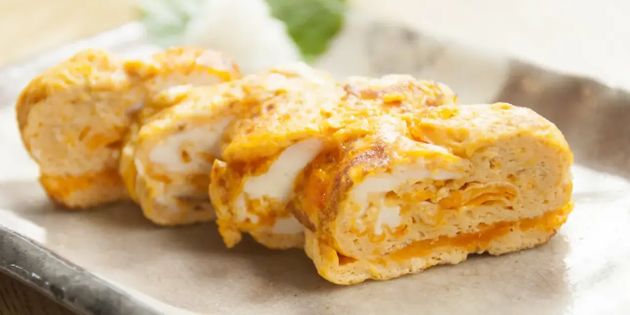 Délicieux oeuf japonais roulé, aux couches dorées et blanches, servi sur une assiette avec une feuille verte.
