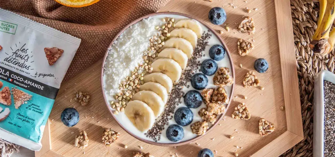 Un bol de smoothie aux bananes, myrtilles, noix de coco râpée et graines de chia, parfait pour un déjeuner au bureau sain et gourmand.