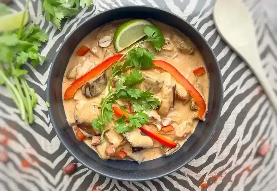 Un délicieux curry rouge, une composition appétissante avec des poivrons, de la coriandre et un quartier de citron vert.