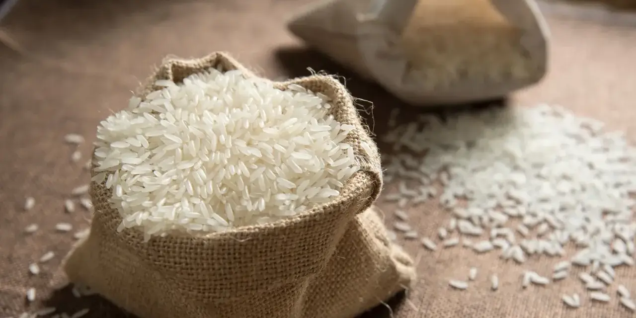 Un sac en toile de jute déborde de riz blanc, une céréale essentielle. Une autre bourse de riz est visible en arrière-plan.