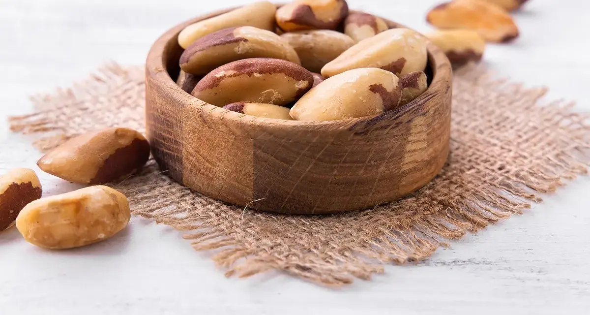 Un bol en bois rempli de noix du Brésil, mettant en avant leurs bienfaits nutritionnels. Quelques noix sont dispersées autour.