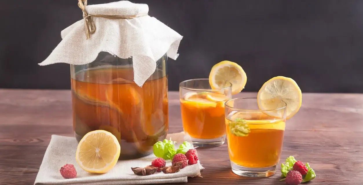 Bocal de kombucha et deux verres garnis de citron, framboises et menthe. Découvrez les kombucha bienfaits pour une boisson rafraîchissante et saine.