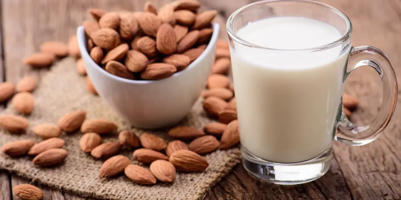 Un verre de lait d'amande frais à côté d'un bol d'amandes entières sur une surface en bois rustique.