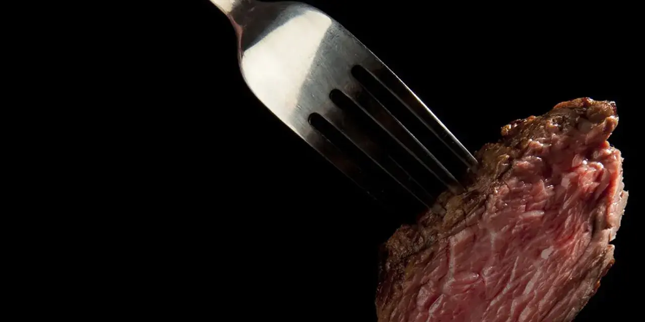 Une fourchette transperce un morceau de viande rouge, rappelant la prudence pour ceux qui ont une allergie au porc.