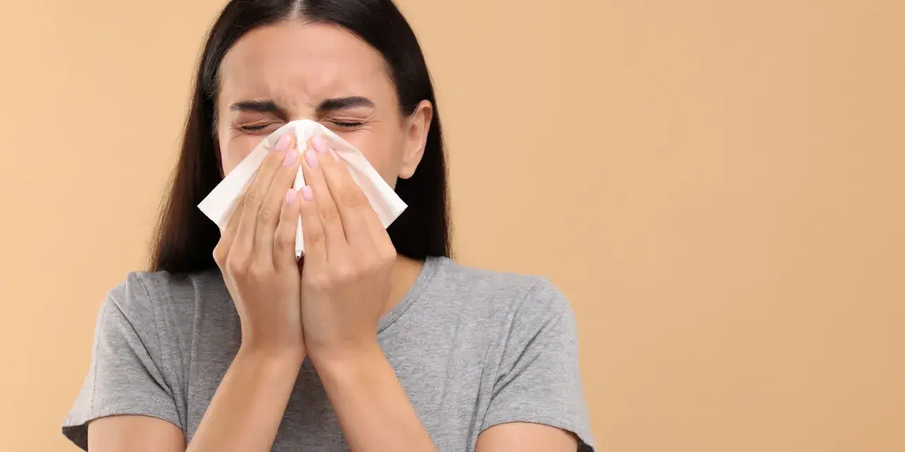 Une jeune femme se mouche dans un mouchoir en papier, le nez bouché par un rhume.