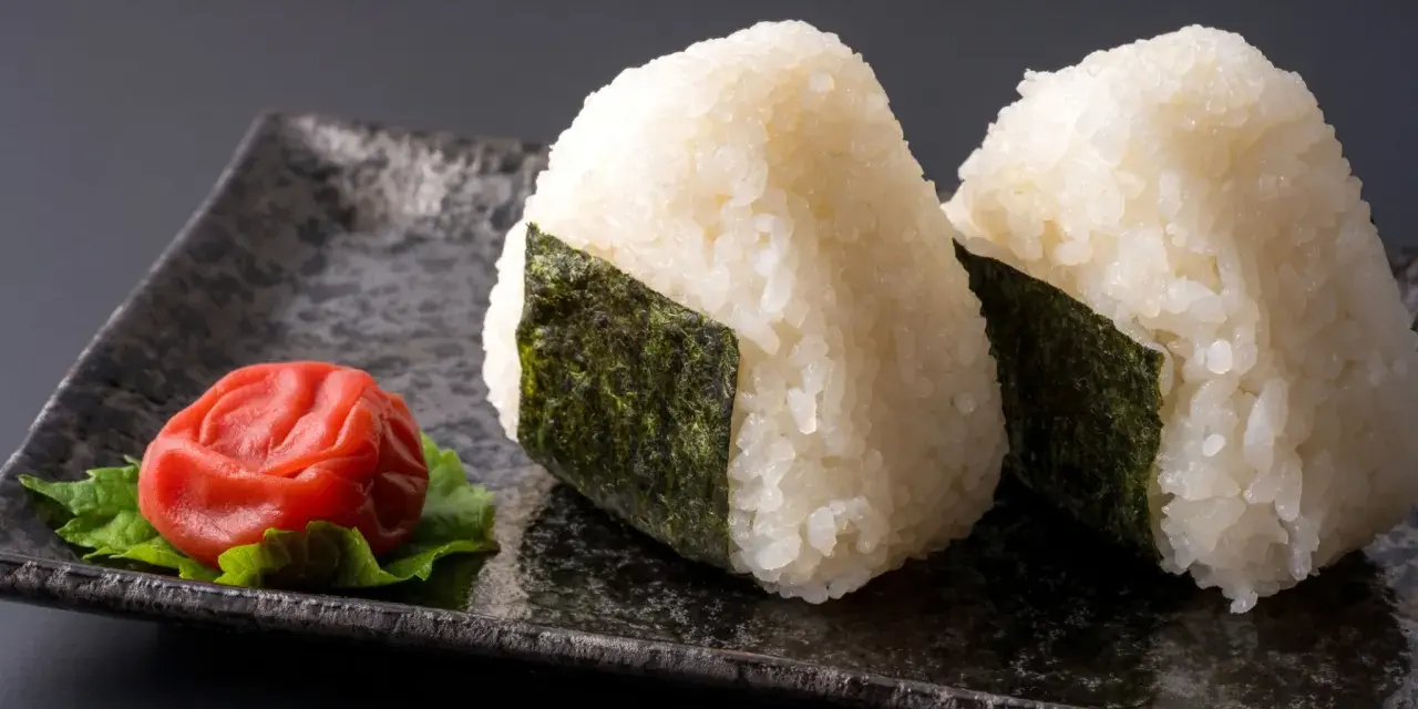 Deux onigiri algue sur une assiette avec une prune salée.