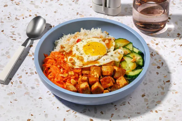 Un bol de bibimbap tofu avec riz, carottes râpées, concombre, œuf au plat et cacahuètes concassées.