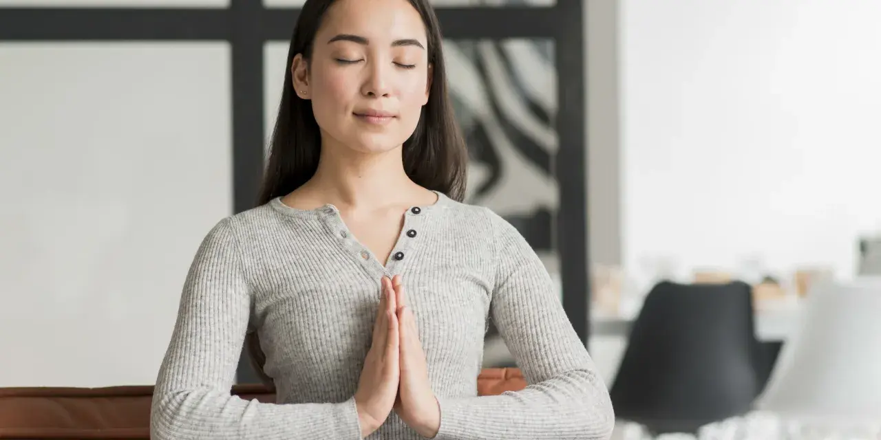 Jeune femme méditant, mains jointes, pour apprendre comment reduire le stress naturellement.