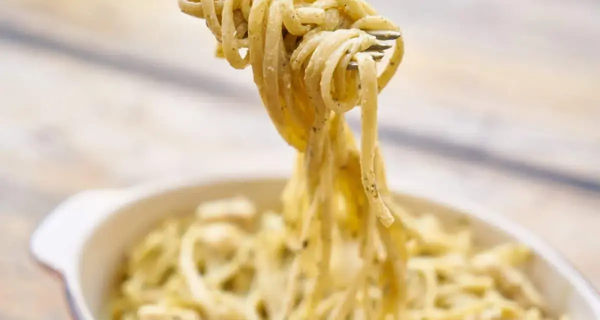 Une fourchette soulève des pâtes crémeuses, peut-être des pâtes cacahuète, d'un plat.